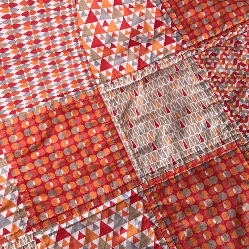 May include: A patchwork quilt with a variety of geometric patterns in shades of orange, brown, and white. The quilt is made of different fabrics with different textures.