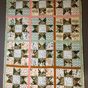 May include: A green, brown and white patchwork quilt with a star pattern. The quilt is made of different fabrics with floral and botanical prints. The quilt is hanging on a wall.