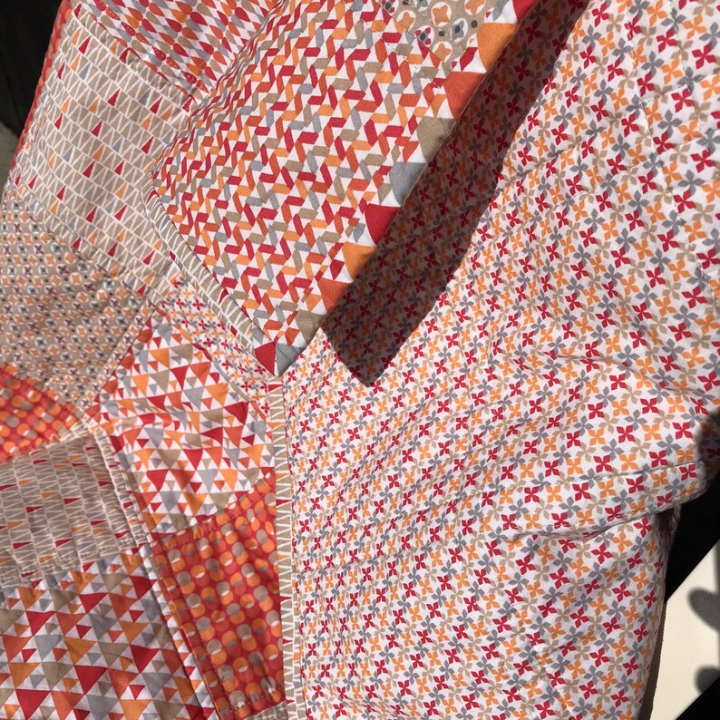 May include: A patchwork quilt with a variety of geometric patterns in shades of red, orange, and gray. The quilt is made of cotton fabric and has a soft, comfortable feel.