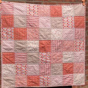May include: A patchwork quilt with a variety of geometric patterns in shades of orange, red, and white.