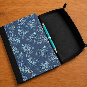 May include: A rectangular folding tray with a dark blue fabric exterior featuring a white coral pattern and two silver metal snaps. The interior is lined with solid black fabric, and a turquoise and silver ballpoint pen rests inside.
