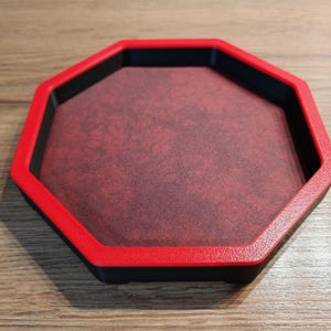 May include: An octagonal tray with a red rim and a black base. The interior has a textured, reddish-brown surface. The tray is designed to hold small items.