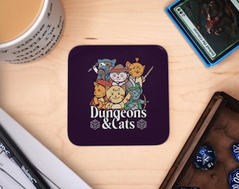 Może przedstawiać: Kwadratowa, fioletowa podstawka z kreskówkową ilustracją kotów w kostiumach fantasy. Tekst "Dungeons & Cats" znajduje się poniżej. W tle widoczny jest kubek, kości i karta.