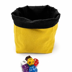 May include: A fabric pouch with a bright yellow exterior and a black interior lining. In front of the pouch sits a small cluster of multi-coloured polyhedral dice, including a purple glitter die, a white die, a yellow die, a red die, and a blue die.