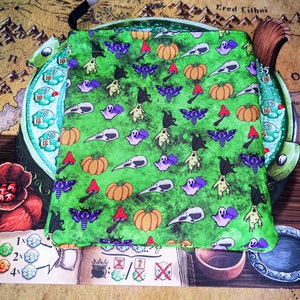 以下が含まれることがあります： 緑色の布製のポーチで、ハロウィンをテーマにしたプリントが施されています。かぼちゃ、幽霊、蛾、頭蓋骨が描かれています。ポーチは柔らかく、質感のある布地で作られています。