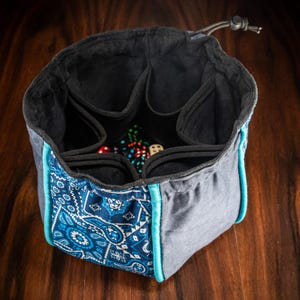 Premium XL dice bag with suede-lined interior, roomy freestanding square base and handy outer pockets for sorting dice, coins, markers and gaming tokens – handmade in the UK.
Perfect for Game Masters, Dungeon Masters, RPG adventurers and tabletop hobbyists playing D&D, Pathfinder 2e, Warhammer 40k, Kill Team, Blood Bowl, Arkham Horror LCG, Marvel Champions LCG, Gloomhaven & Frosthaven, Nemesis, Spirit Island, Scythe, Brass Birmingham, Terraforming Mars and more.