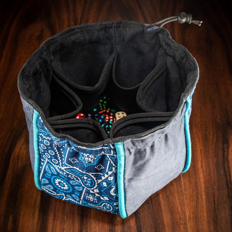 Premium XL dice bag with suede-lined interior, roomy freestanding square base and handy outer pockets for sorting dice, coins, markers and gaming tokens – handmade in the UK.
Perfect for Game Masters, Dungeon Masters, RPG adventurers and tabletop hobbyists playing D&D, Pathfinder 2e, Warhammer 40k, Kill Team, Blood Bowl, Arkham Horror LCG, Marvel Champions LCG, Gloomhaven & Frosthaven, Nemesis, Spirit Island, Scythe, Brass Birmingham, Terraforming Mars and more.