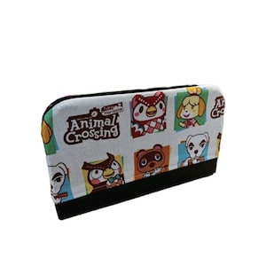 Può includere: Un astuccio rettangolare bianco con un motivo colorato di personaggi di Animal Crossing. L'astuccio ha una base nera e una chiusura a cerniera. Il testo "Animal Crossing New Horizons" è stampato sul davanti.