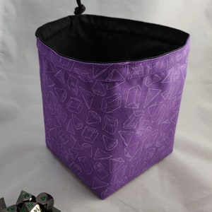 May include: Purple dice bag with a white geometric pattern and a black drawstring. The bag is filled with metal dice with green numbers.