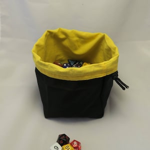 May include: A black fabric dice bag with a yellow lining. The bag is open and filled with colorful dice. A group of dice are scattered on a white surface.