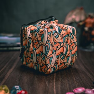 May include: A drawstring dice bag with a colorful banana pattern. The bag is made of fabric and has a black drawstring.