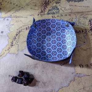 May include: A blue and black dice tray with a geometric pattern. The tray is made of leather and has a soft, velvety lining. There are several black dice with red numbers on the tray.