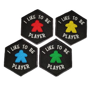 May include: Four black hexagonal patches with white text that reads "I like to be a player". Each patch features a different colored game piece in the center: red, yellow, blue, and green.