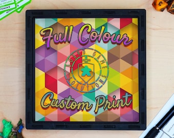 May include: A square black dice tray featuring a colorful geometric pattern background. The text "Full Colour" and "Custom Print" are printed in a stylized font, with a central circular logo containing a shield, sword, and meeple icon.