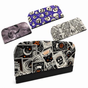 May include: Four rectangular fabric covers with rounded top corners. One features a black, white, and orange tarot card print with a cat and skull. Another has a purple skull pattern. One shows a moon and bats. The last has a white floral skull print.