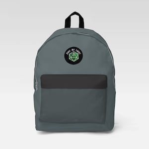 Könnte beinhalten: Ein grauer Rucksack mit einer schwarzen Tasche und einem schwarzen und grünen gestickten Aufnäher mit der Aufschrift "Just My Luck!" mit einem grünen Würfel mit einer weißen "1" darauf.