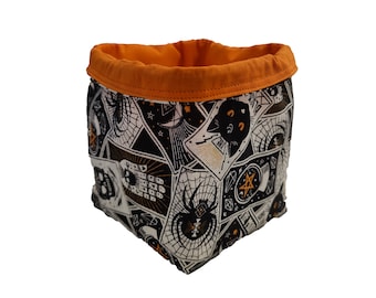 May include: A fabric storage basket with a Halloween-themed print. The exterior features a black and white pattern with spiders, cats, and other spooky imagery. The interior and rim are orange.