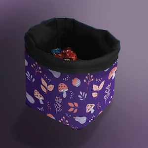 Puede incluir: Bolsa de dados morada con cordón de ajuste negro y un patrón de hongos y hojas. La bolsa está llena de dados de colores.