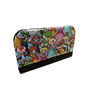 May include: A rectangular clutch featuring a colorful print of various characters from the Super Mario video game series. The design includes Mario, Luigi, Princess Peach, Yoshi, and Bowser, set against a light blue background. The bottom is black.