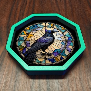 May include: An octagonal tray with a bright teal rim featuring a circular insert. The insert displays a black raven perched against a background of stained glass in shades of blue, purple, yellow, and white with a geometric leaded pattern.