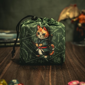 May include: Green drawstring bag with a cat wearing a blue and red samurai outfit and holding swords. The bag has a white background with a pattern of swords and axes.