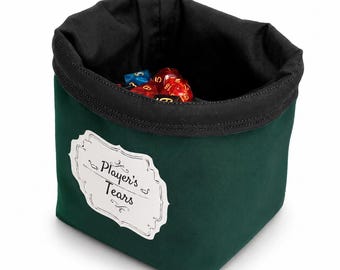 May include: A dark green fabric dice bag with a black interior lining. The exterior features a white rectangular label with decorative borders and the black printed text Player's Tears. Several multi-coloured polyhedral dice are inside the bag.