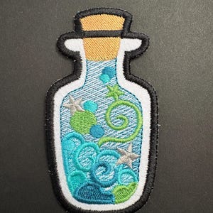 May include: Embroidered patch in the shape of a potion bottle. The bottle features a blue and teal design with green swirls, stars, and bubbles. The bottle has a white border with a black outline and a cork top.