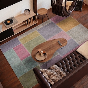 Könnte beinhalten: Ein Wohnzimmer mit einem braunen Ledersofa, einem hängenden Korbstuhl, einem Plattenspieler und einem bunten Teppich. Der Raum hat Holzböden und ein großes Fenster.