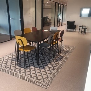 Puede incluir: Una moderna sala de reuniones de oficina con una mesa rectangular oscura rodeada de ocho sillas coloridas. Las sillas son en tonos de amarillo, gris y burdeos. Una alfombra estampada se encuentra debajo de la mesa, y paredes de vidrio en el fondo.