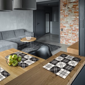 May include: Two black and white plaid placemats on a wooden table in a modern kitchen. The placemats are made of a woven fabric and have a checkered pattern. There are green apples in a bowl on the table.