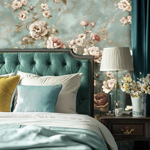 May include: A teal velvet headboard with a tufted design, a white and blue pillow, and a yellow pillow. The headboard is in front of a wall with a floral wallpaper pattern. A lamp with a white shade is on a nightstand next to the bed.