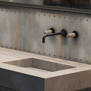 May include: A modern bathroom sink with a concrete countertop and a black faucet mounted on a wall with a rusty metal finish. The wall is decorated with small metal rivets.