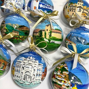 K&ouml;nnte beinhalten: Eine Sammlung von neun kugelf&ouml;rmigen Glasornamenten, die jeweils handbemalt mit detaillierten Szenen europ&auml;ischer Landschaften und Wahrzeichen sind, darunter der Trevi-Brunnen in Rom und Positano, verziert mit wei&szlig;en und goldenen Schleifen.