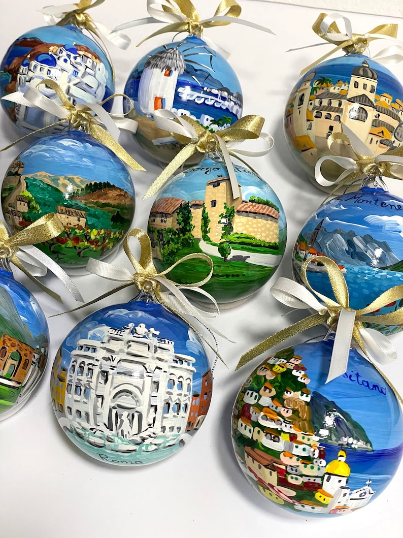 K&ouml;nnte beinhalten: Eine Sammlung von neun kugelf&ouml;rmigen Glasornamenten, die jeweils handbemalt mit detaillierten Szenen europ&auml;ischer Landschaften und Wahrzeichen sind, darunter der Trevi-Brunnen in Rom und Positano, verziert mit wei&szlig;en und goldenen Schleifen.