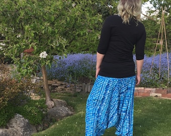 May include: A person wearing blue and white patterned pants with a black long-sleeved shirt. The person is standing in a garden with green grass and blue flowers.