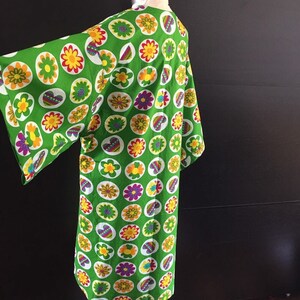 K&ouml;nnte beinhalten: Ein gr&uuml;nes Kimono mit einem bunten Blumenmuster. Das Kimono hat einen weiten, flie&szlig;enden &Auml;rmel und eine lockere Passform.