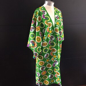 K&ouml;nnte beinhalten: Ein gr&uuml;nes Kimono mit einem farbenfrohen Blumenmuster. Das Kimono hat einen V-Ausschnitt und lange &Auml;rmel. Das Muster zeigt Kreise mit Blumen und Schmetterlingen.
