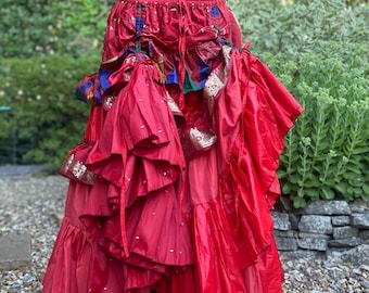 May include: A vibrant red skirt with multiple layers and decorative accents. The skirt features a ruffled design with gold and colorful embellishments. The waistline is elasticized. The skirt is made of a flowing fabric.