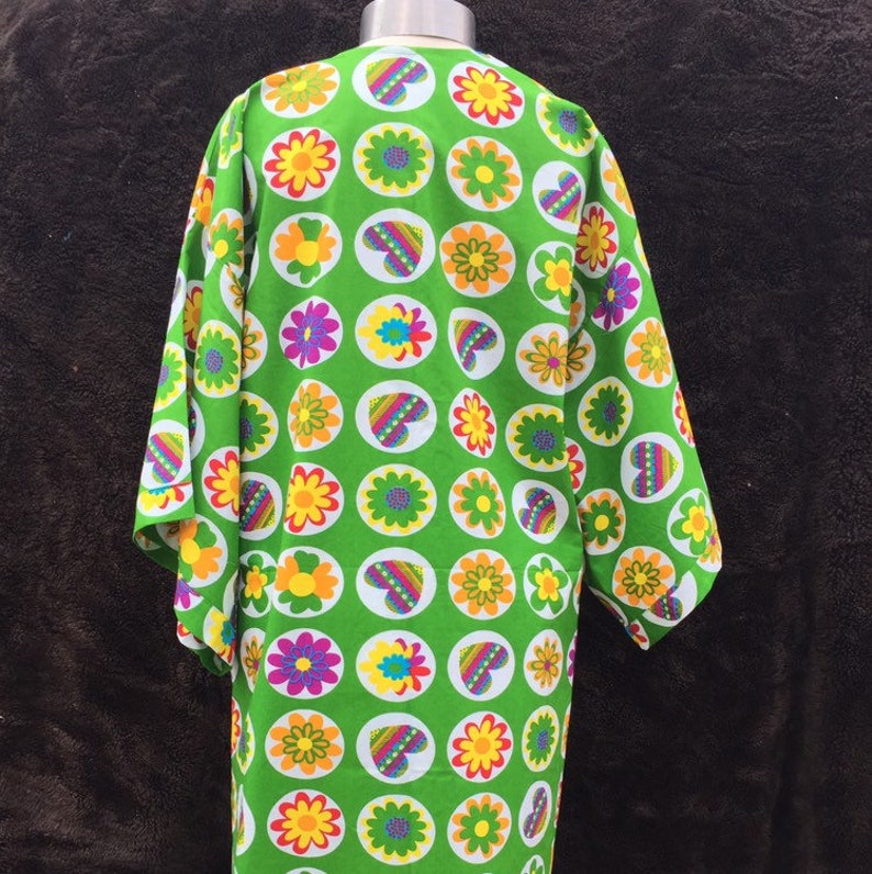 K&ouml;nnte beinhalten: Eine gr&uuml;ne Robe mit wei&szlig;em Hintergrund und einem Muster aus bunten Blumen und Herzen in Kreisen.