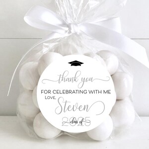 May include: White favor bags filled with white candy and a round white sticker with black text that says "Thank you for celebrating with me, Love, Steven, Class of 2025".