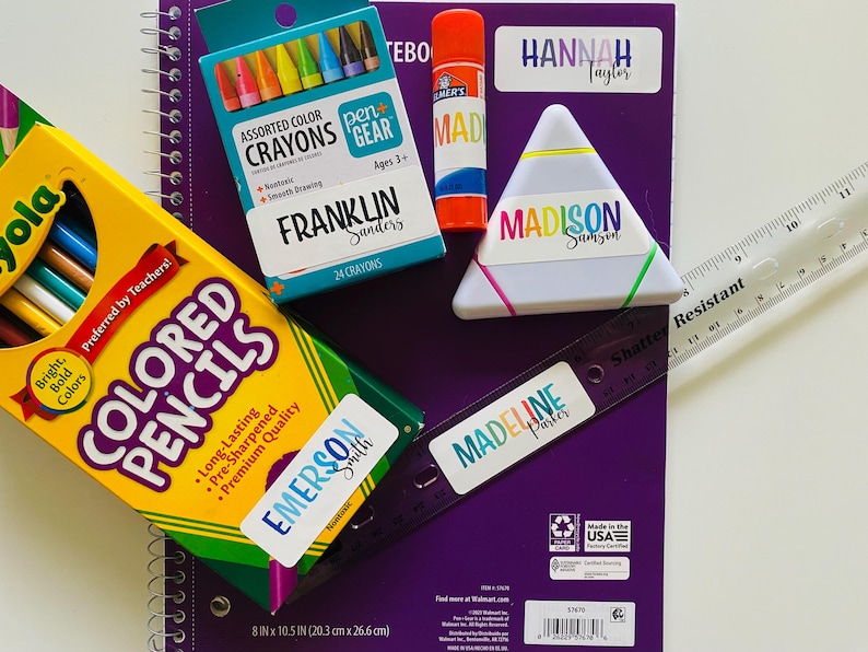 Pu&ograve; includere: Una collezione di materiale scolastico che include un quaderno a spirale viola, una scatola di matite colorate Crayola, una scatola di pastelli a cera Pen+Gear, una colla stick Elmer's, un astuccio triangolare bianco e un righello di 30 cm.