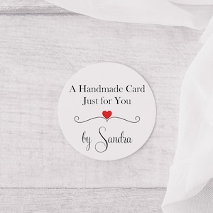 May include: A white circle sticker with black text that reads "A Handmade Card Just for You" with a red heart and the name "Sandra" in cursive.