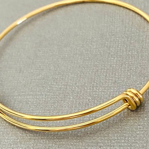 May include: A gold-toned expandable bangle bracelet with a double-wire design and a knotted closure.