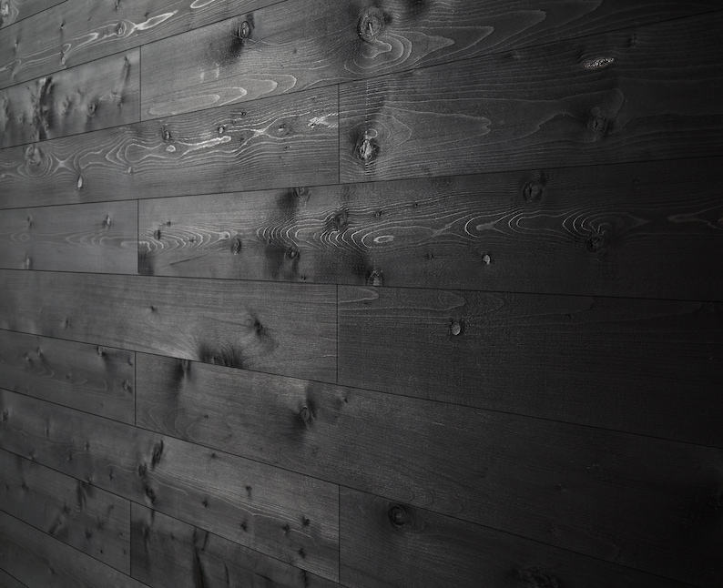 Puede incluir: Una pared cubierta de tablones de madera oscura, creando un aspecto r&uacute;stico y moderno. Los tablones est&aacute;n dispuestos en un patr&oacute;n horizontal, con la veta de la madera visible. La madera tiene una mancha oscura, casi negra, que le da un aspecto elegante y sofisticado.