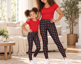 May include: Matching outfits consisting of solid red short-sleeved t-shirts and black leggings featuring a repeating pattern of white polka dots and small red bows. The leggings are full-length and fitted, paired with plain white sneakers.