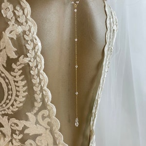 May include: A delicate gold back necklace with a teardrop crystal pendant and smaller crystals along the chain.