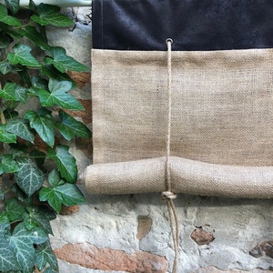 May include: A brown and black fabric shade with a rope pull. The shade is rolled up and hanging from a wall.