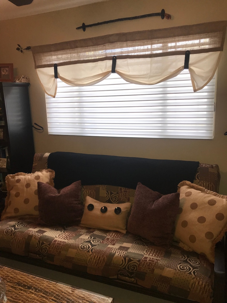 Pu&ograve; includere: Un divano futon marrone con una trapunta trapuntata e diversi cuscini. I cuscini sono marroni, beige e beige chiaro con pois e bottoni decorativi. Il futon &egrave; davanti a una finestra con una bordura bianca e un top in juta marrone.