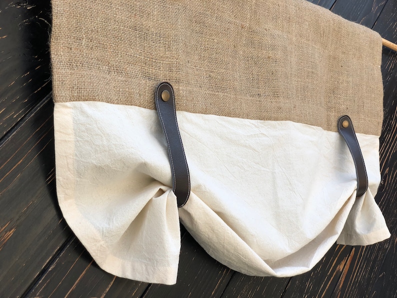 Pu&ograve; includere: Una tenda a valance in tessuto bianco con lacci in pelle marrone e un retro in juta. La valance &egrave; raccolta e legata indietro su entrambi i lati.