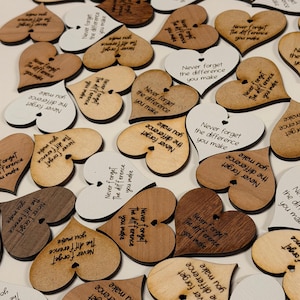 May include: A collection of heart-shaped wooden cutouts in various shades of brown and white. Each heart is engraved with the phrase "Never forget the difference you make". These decorative pieces are ideal for crafts or personalized gifts.